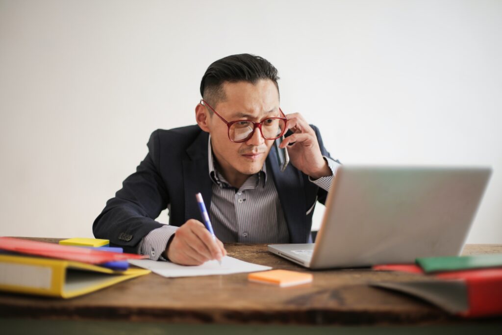Employee Multi-tasking between writing, talking and looking at a laptop.